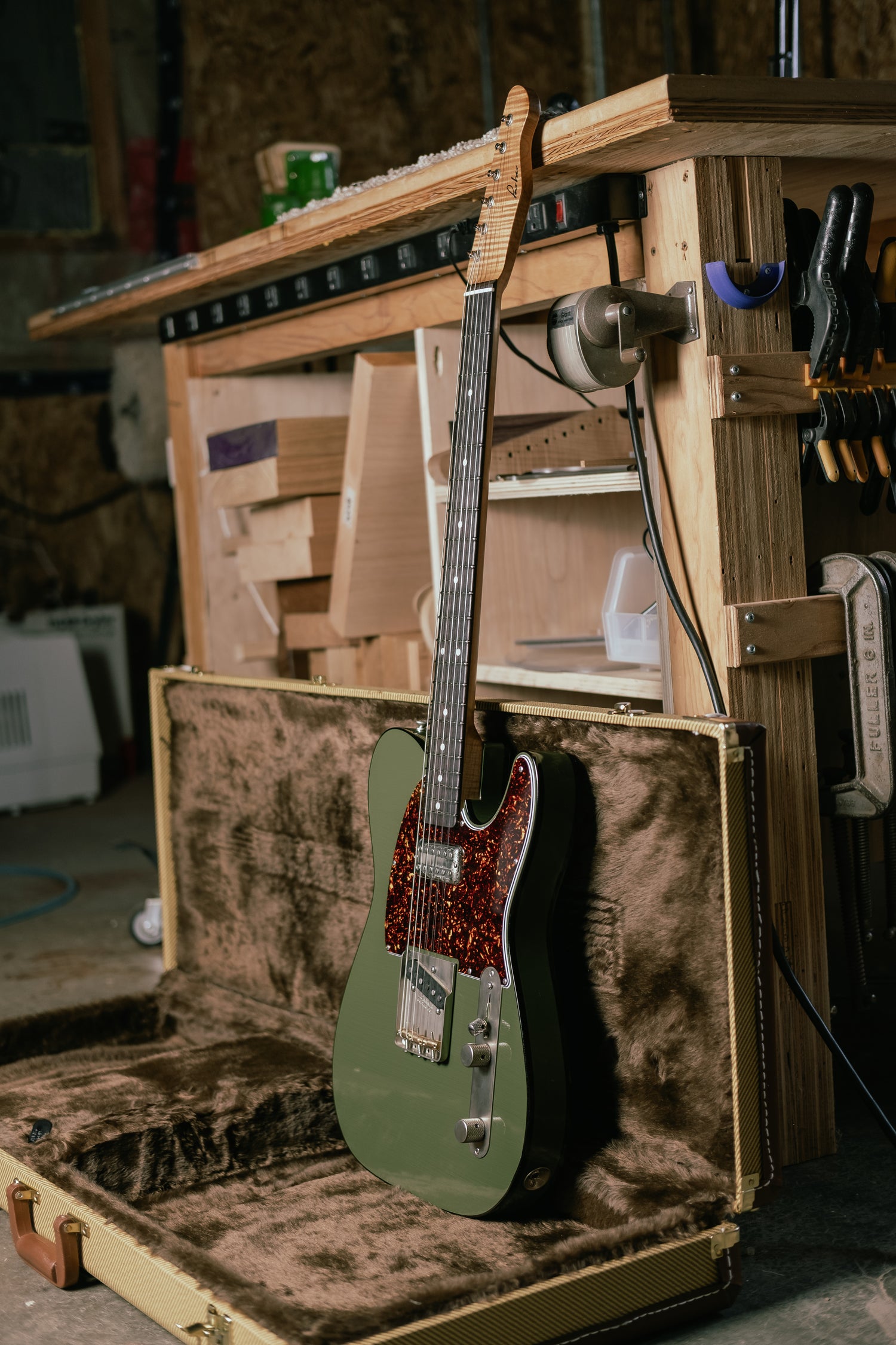Green electric guitar in an open case with a workshop background